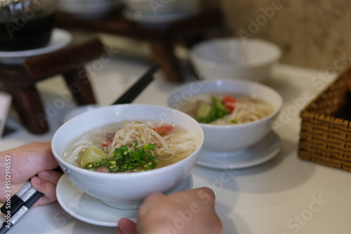 Fototapeta Naklejka Na Ścianę i Meble -  Vietnamese pho soup seller preparing rice vermicelli soup on the street small eatery cooking fa soup in Vietnam street food dirt unsanitary conditions delicious travel tourists local. population.