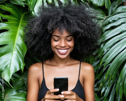 Woman with curly hair smiles, looking at phone in tropical leaves