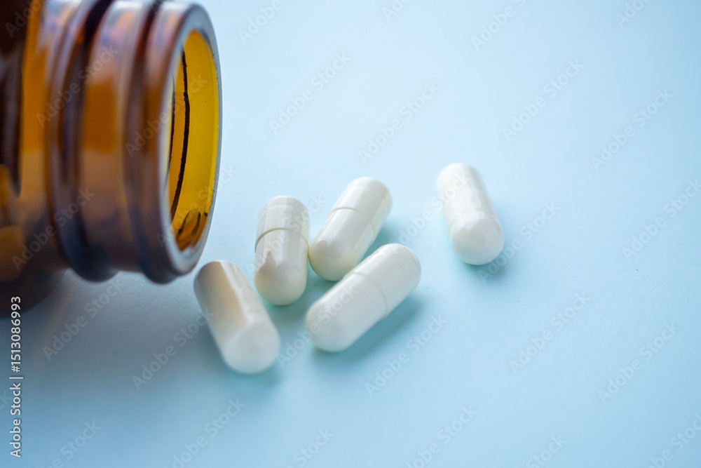 Naklejka premium medicine pills capsule spilling out of bottle on blue background