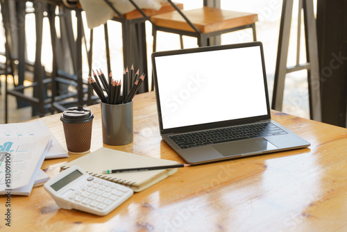 Mockup image of laptop computer screen with blank white background for advertising text on a large wooden table with office supplies at a bright modern workplace. Marketing and business concept.
