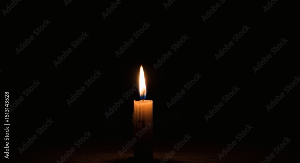 Fototapeta premium A single candle flame burning brightly in the darkness casting a soft glow around the wax candle body
