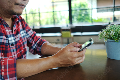 An elderly Asian man in a red plaid shirt happily uses his phone for the first time in a coffee shop.