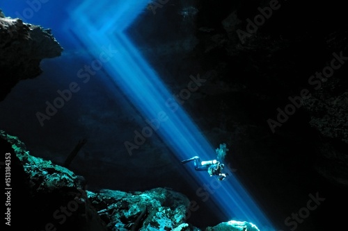 Scuba diver swimming underwater in the sun beams. Large cenote cave with blue light rays and scuba diver.  Explorer diving in the dark cave, travel picture. Cenote and diver