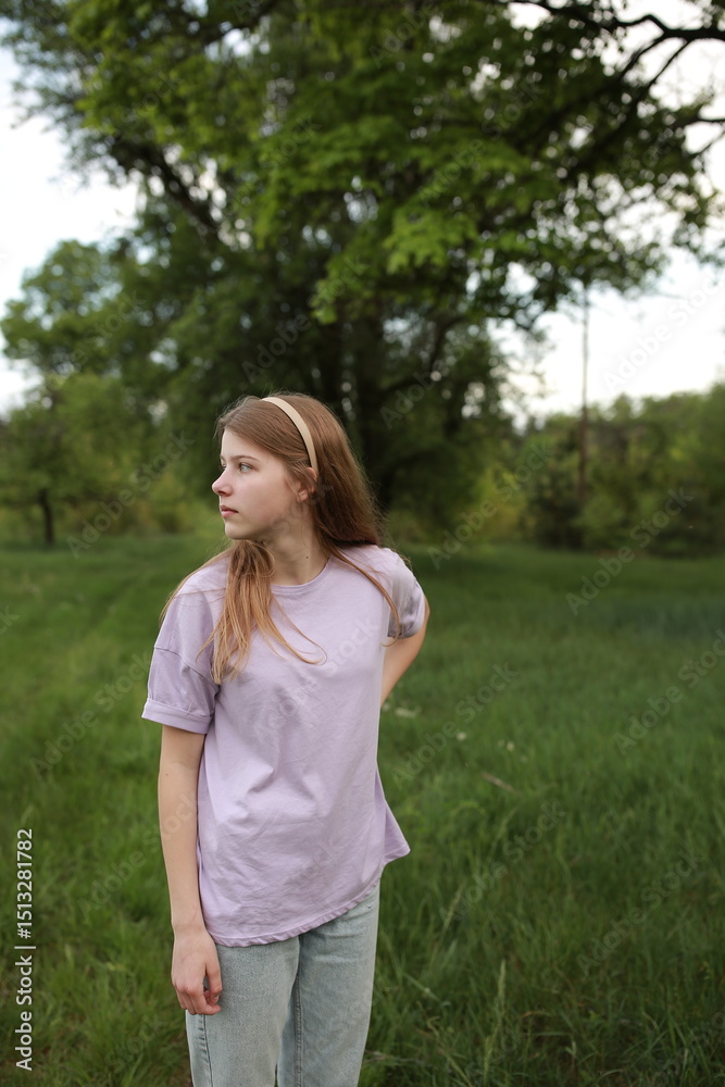 Teen girl smiling while standing on a green meadow in the park. Peaceful spring day with natural background and casual outdoor vibes. Smiling teenage girl posing in nature wearing casual clothes. Teen girl smiling while standing on a green meadow in the park. Peaceful spring day with natural background and casual outdoor vibes. Smiling teenage girl posing in nature wearing casual clothes.
