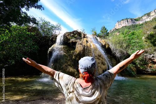Mujer de 58 años con los brazos en cruz de espalda a la cámara en un salto de agua, en Cortes de Pallas Comunidad Valenciana