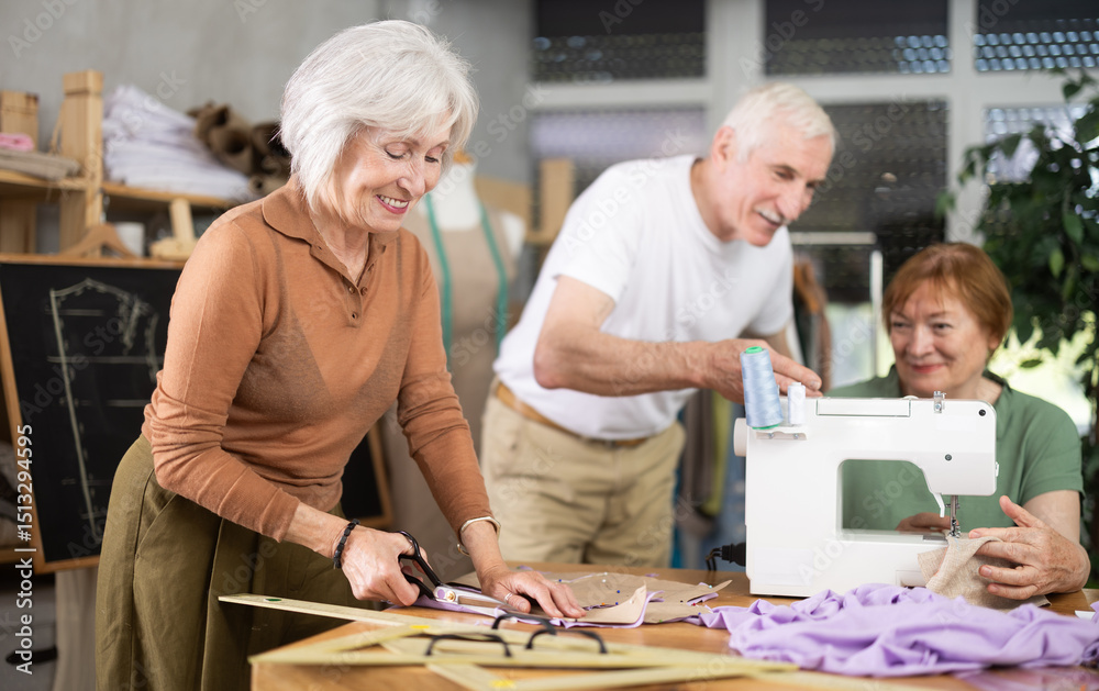 Obraz premium Smiling older woman using scissors to cut fabric pieces along pinned pattern during sewing session for seniors in shared learning space