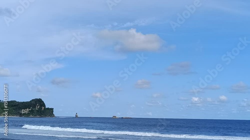 Beautiful coastal view with gentle waves lapping the shore. A serene island backdrop under a bright sky and light clouds makes for a perfect landscape.
