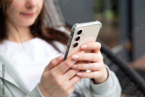 Young woman using Samsung Galaxy S23 FE smartphone indoors, browsing or texting in a relaxed and modern environment.