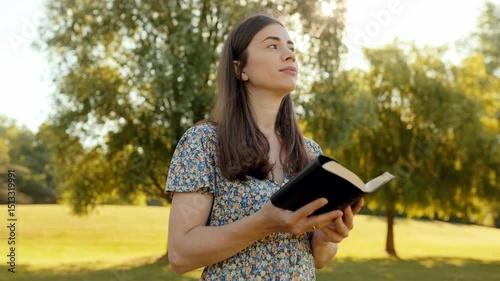 Woman standing in sunny meadow holding Bible, reading and smiling with eyes lifted to sky, slow motion, spiritual connection, peaceful nature, sunlight, faith, joy, outdoor inspiration, serenity