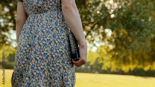 Slow motion close-up of Bible in woman’s hand as she walks through golden meadow, cinematic shot, soft sunlight, emotional scene, spiritual symbolism, dreamy summer landscape