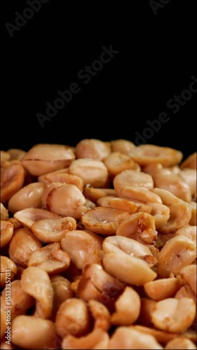 Detail of roasted peanuts peeled rotating on black background. Suitable for advertising or promotion. Vertical shot