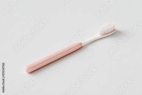 A pale pink and white toothbrush lies diagonally on a plain white background.  Its bristles are slightly splayed