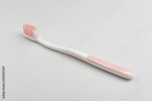 A single, new toothbrush with a white handle and pale pink accents rests on a plain white background.  The bristles are two-toned, white and pink photo