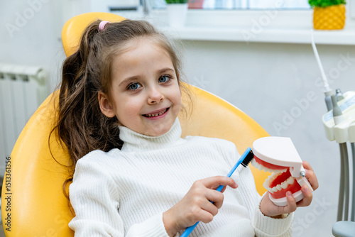 Girl is practicing how to properly brush her teeth. Good oral hygienist with jaw model teaching patient to clean teeth properly to prevent caries, keep teeth healthy and have beautiful smile.