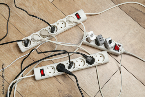Fotografie Extension power boards overloaded with plugs on wooden floor, top view