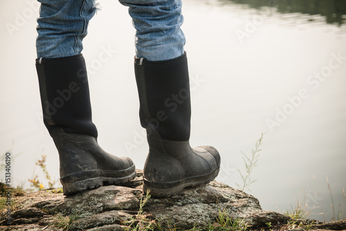 Feet and boots of a fisherman standing on the edge of a lake 