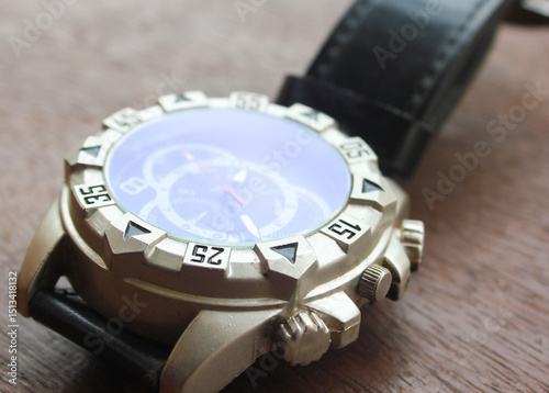 Luxury analog wristwatch with a black leather strap and stainless steel bezel, placed on a wooden surface, showcasing bold numerals and a modern chronograph dial.