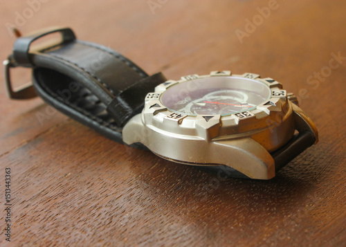 Luxury analog wristwatch with a black leather strap and stainless steel bezel, placed on a wooden surface, showcasing bold numerals and a modern chronograph dial.