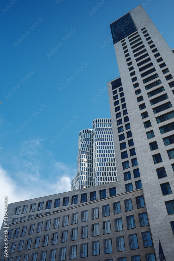 Obraz premium Low angle exterior view of the contemporary white curved skyscraper and modern commercial buildings against a blue sky in Berlin Germany during daytime. 