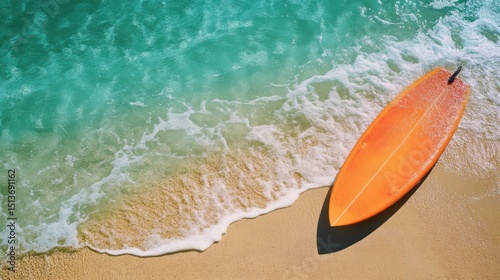 Aerial view of an orange surfboard resting on sun-kissed sand, next to turquoise waves