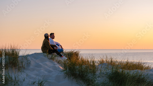 Quadro su tela Friends relaxes on soft sand dunes while watching a breathtaking sunset over the tranquil waters of Denmark coastline