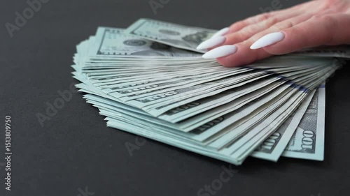 A girl's hand lays out $100 bills on a table. Hundred dollar bills.
