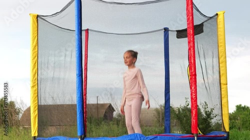 A young girl in pink clothing sits on a trampoline with a safety net in a grassy outdoor area, holding her side with a pained expression.