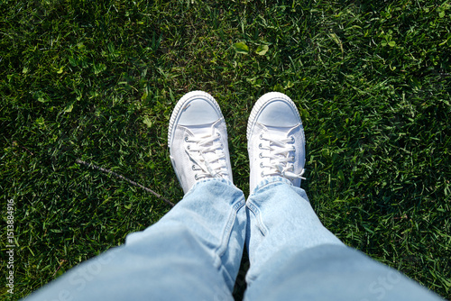 A man in white sneakers stands on green grass, a view from above