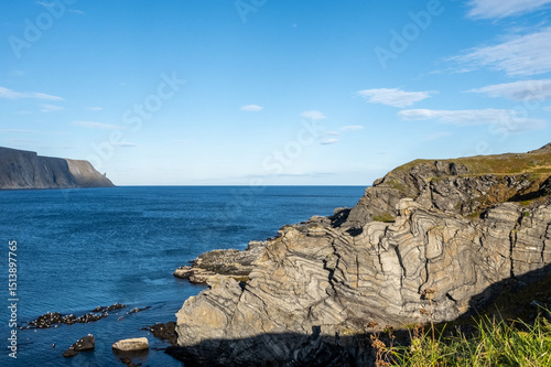  Dramatic rock formations and coastal cliffs at Kirkeporten viewpoint near Skarsvåg, Norway, close to North Cape. Stunning geological patterns meet Arctic Ocean under a clear blue sky photo