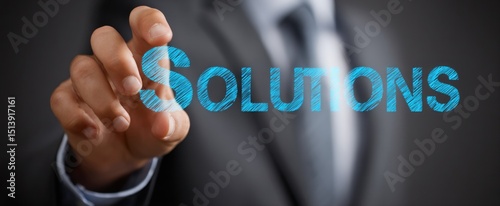 Hand touching the word solutions written in blue against a dark suited person background