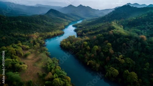 Aerial view of a winding river flowing through a lush green valley surrounded by rolling mountains under a cloudy sky