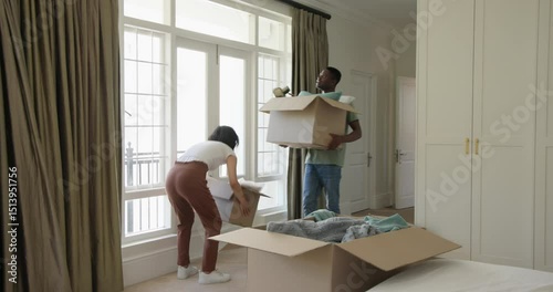 Asian Korean and African American couple entering bedroom with boxes, unpacking bedding for setup