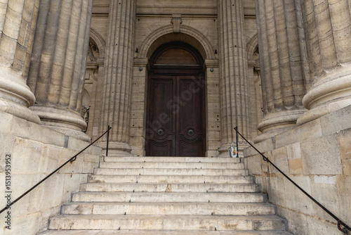 Les escaliers en pierre mènent à une porte en bois ornée, située dans un édifice historique de Paris, Saint-Sulpice.