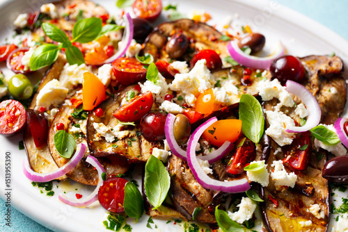 Grilled eggplants salad with feta cheese and tomatoes on a white plate. Close up.