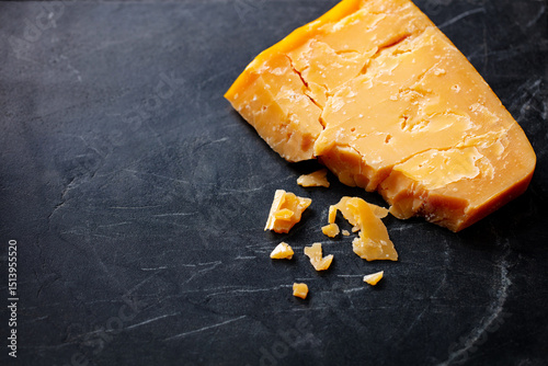 Cheddar cheese on black marble cutting board. Dark background. Copy space. Close up.