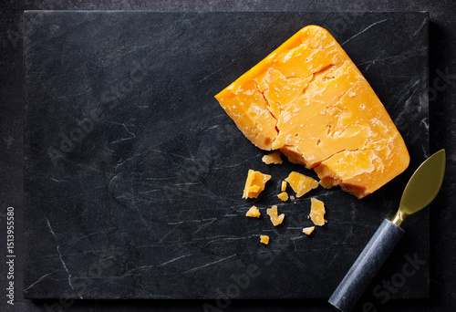 Aged cheddar cheese with knife on black marble serving board. Dark background. Copy space. Top view.