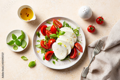 Traditional Italian cuisine. Caprese salad with tomatoes, mozzarella cheese and fresh basil. Beige background. Close up. Top view.
