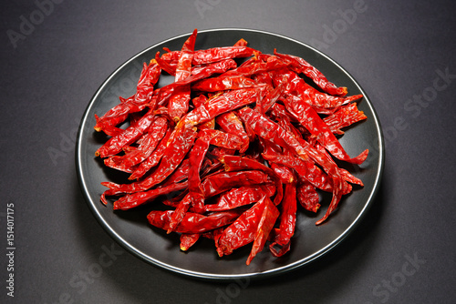 Fototapeta Naklejka Na Ścianę i Meble -  Heap of dry red chilies over black ceramic plate isolated on dark background close-up view 