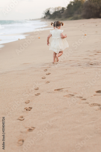 Little cute girl in a white dress with two ponytails on her head plays on the beach in the summer at sea. Child. Baby. Summer