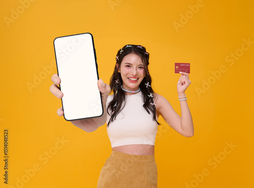 Happy beautiful young Asian woman showing smartphone mockup blank screen and credit card online shopping isolated on yellow background.
