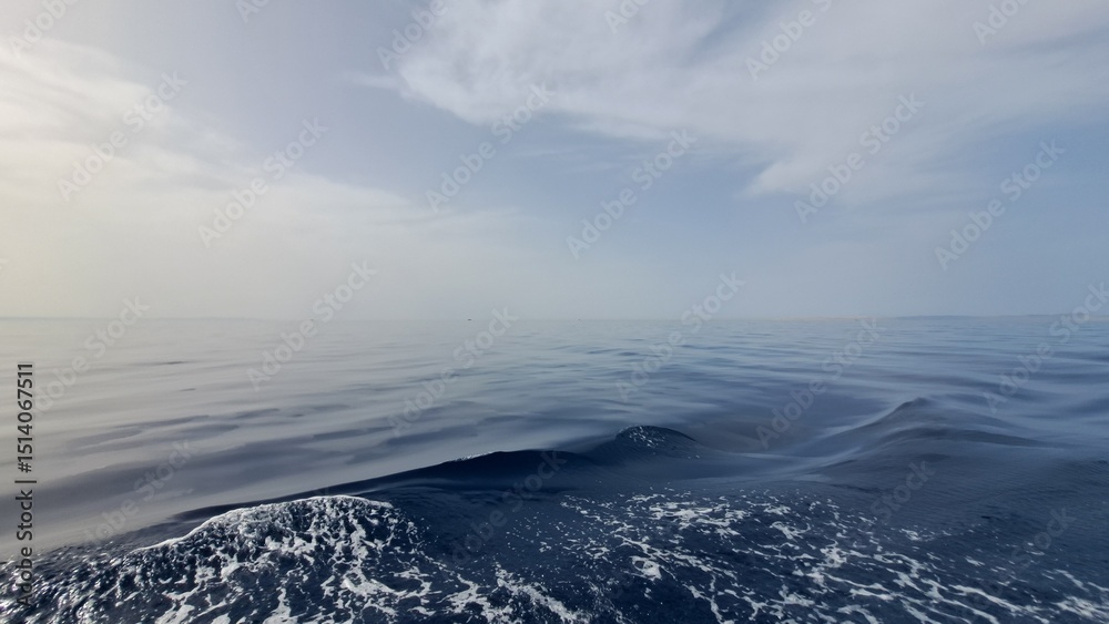 Obraz premium Expansive view of calm ocean waters under a soft blue sky, with gentle waves creating a serene atmosphere, reflecting tranquility and natural beauty in the vast seascape