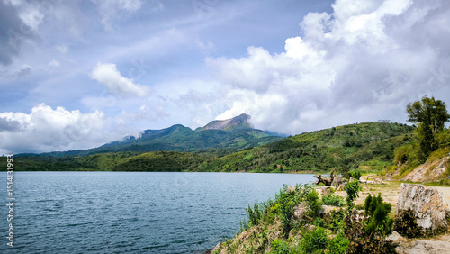 Foto Scenic view of a clear lake surrounded by green hills and a partly cloudy sky with distant mountains in the background