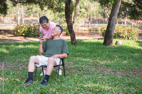 Retired couple video chatting on the phone in a park, smiling happily on a weekend getaway.