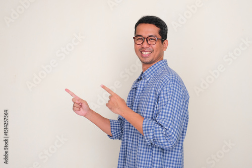 Side view of adult asian man smiling with hands pointing beside photo