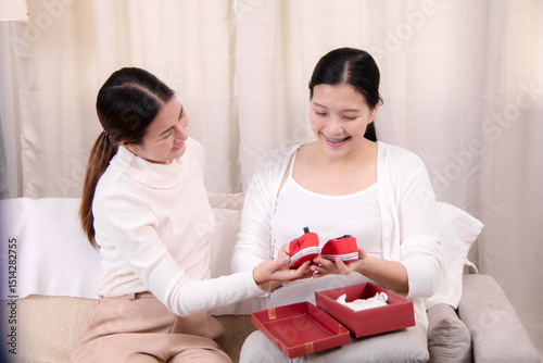 Asian pregnant woman smiling receives a gift from her partner, celebrating love and togetherness, perfect for content related to baby showers, family care, healthcare, friend or family relationships