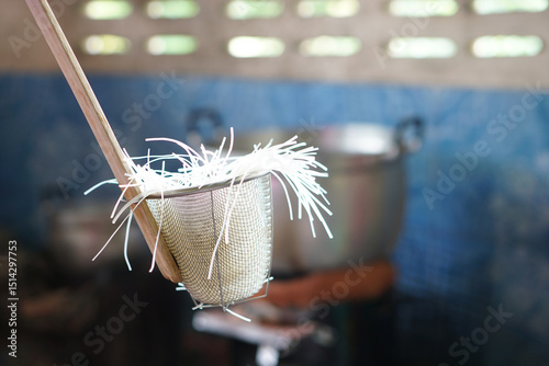 Noodle strainer with rice noodles, used for blanching in hot water. Concept, essential kitchen tool for preparing authentic Asian cooking, ensuring perfect, silky noodles every single time.