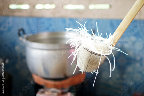 Noodle strainer with rice noodles, used for blanching in hot water. Concept, essential kitchen tool for preparing authentic Asian cooking, ensuring perfect, silky noodles every single time. photo