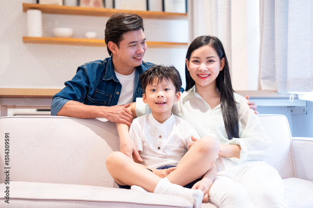 Happy Asian family of three smiling and looking at the camera The parents and a child sit on sofa Happy Asian family of three smiling and looking at the camera The parents and a child sit on sofa