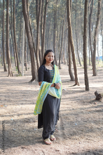 Portrait of a confident Indian woman standing gracefully in a pine forest, dressed in a traditional black kurti with a colorful dupatta
