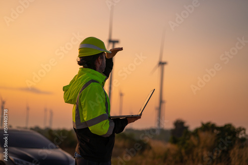 Engineer wearing uniform inspection and survey work in wind turbine farms rotation to generate electricity energy. Maintenance engineer working in wind turbine farm at sunset.